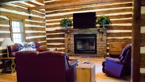 A log cabin interior with a stone fireplace, leather sofas, and a flat-screen TV mounted above the fireplace. - Beautiful secluded Log Home - Nestled in the country! (Wright City)