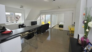 A modern kitchen with a black countertop, bar stools, and a dining area with a yellow chair. - Modern, Architect-Designed Penthouse Loft With 2 Outdoor Roof Terraces (Vienna)