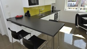 A modern kitchen with a black countertop, white cabinets, and a yellow backsplash. There are two black chairs and a small table with a red object on it. - Modern, Architect-Designed Penthouse Loft With 2 Outdoor Roof Terraces (Vienna)