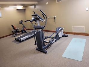 A fitness room with an elliptical trainer, a treadmill, and a yoga mat.