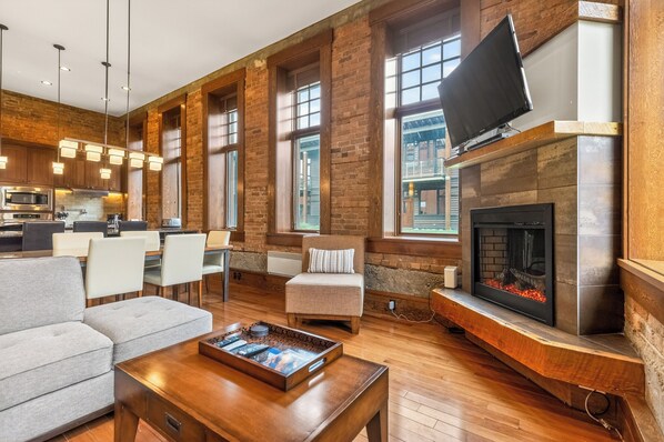 A spacious living area with a fireplace, seating, and a kitchen in the background.
