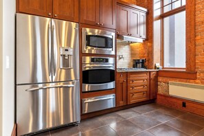 A modern kitchen with stainless steel appliances, wooden cabinets, and a brick wall.