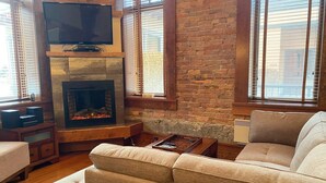 Ein gemütliches Wohnzimmer mit Kamin, einem darüber montierten Flachbildfernseher und einer bequemen Couch.