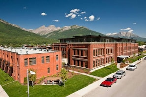 A red brick building with a flat roof and large windows, surrounded by green lawns and a parking area with cars.