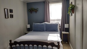 Una camera da letto con un letto grande, due comodini con lampade, una finestra con tende e mensole a parete con piante.