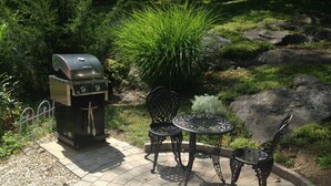 An outdoor patio with a grill, two chairs, and a small table.