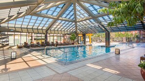 An indoor swimming pool with a glass ceiling, tiled floor, and lounge chairs.