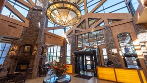 A spacious lobby with a stone fireplace, comfortable seating, a reception desk, and large windows offering views.