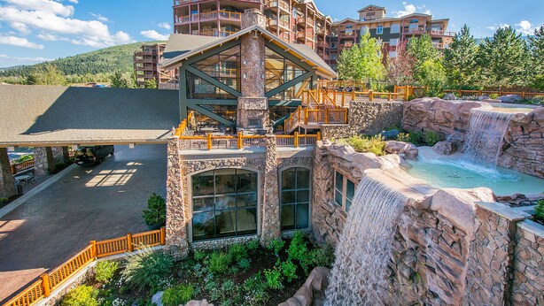 A multi-story hotel with a waterfall feature, outdoor seating, and a view of a mountainous landscape.