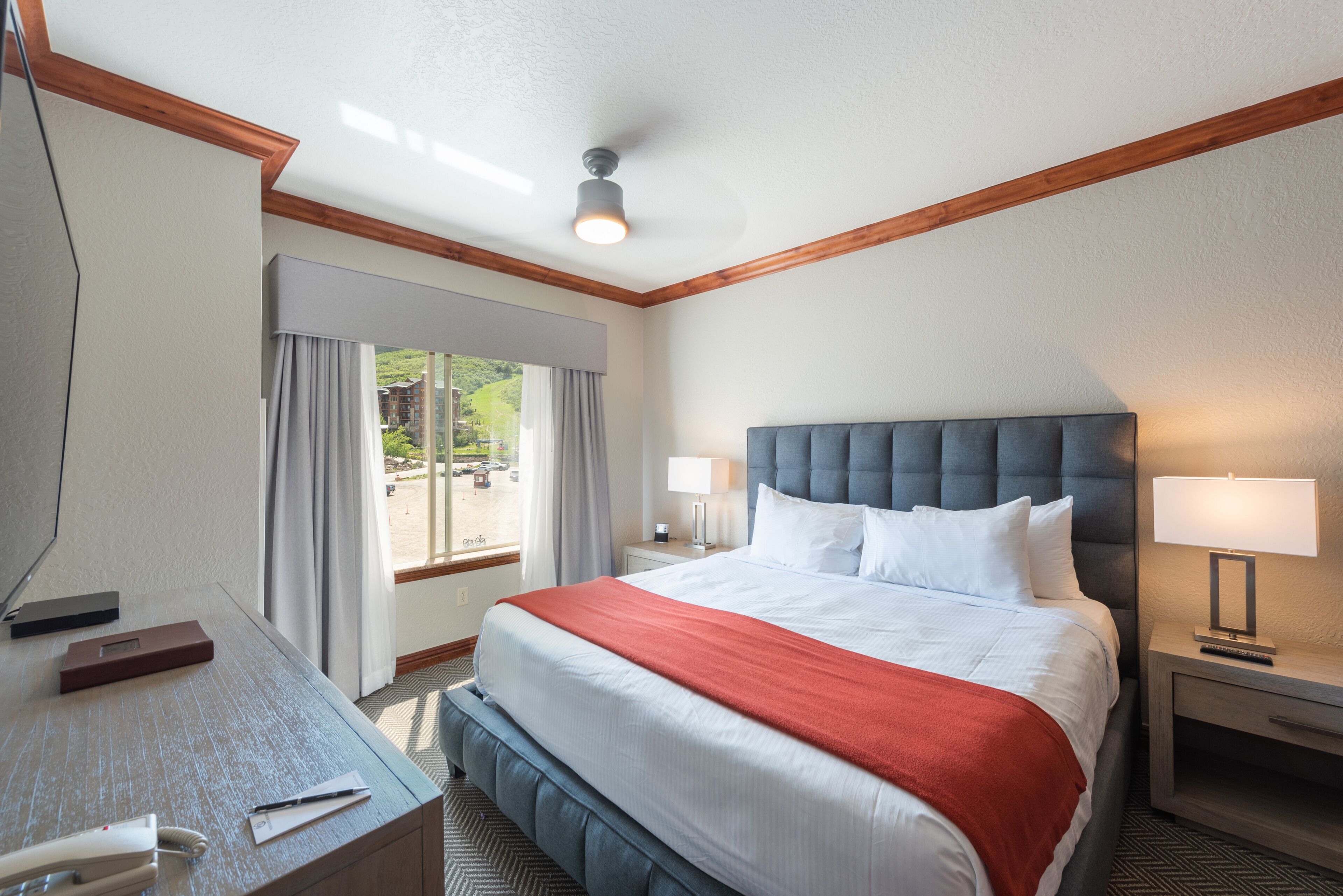 Habitación de hotel con una cama grande, un escritorio, una silla, una mesita de noche y una ventana con cortinas.