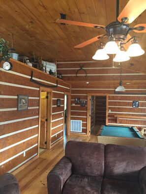 A cozy room with wooden walls, a ceiling fan, a pool table, and a plush sofa.