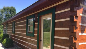 Une cabane en rondins avec une porte verte, de nombreuses fenêtres et un espace extérieur bien visible.