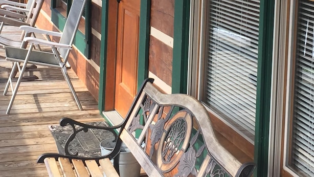 Une véranda en bois avec un banc, une porte décorée d’une guirlande et de grandes fenêtres équipées de stores.