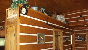 L’intérieur d’un chalet en bois, avec une horloge, un tableau encadré et un panneau portant une citation.