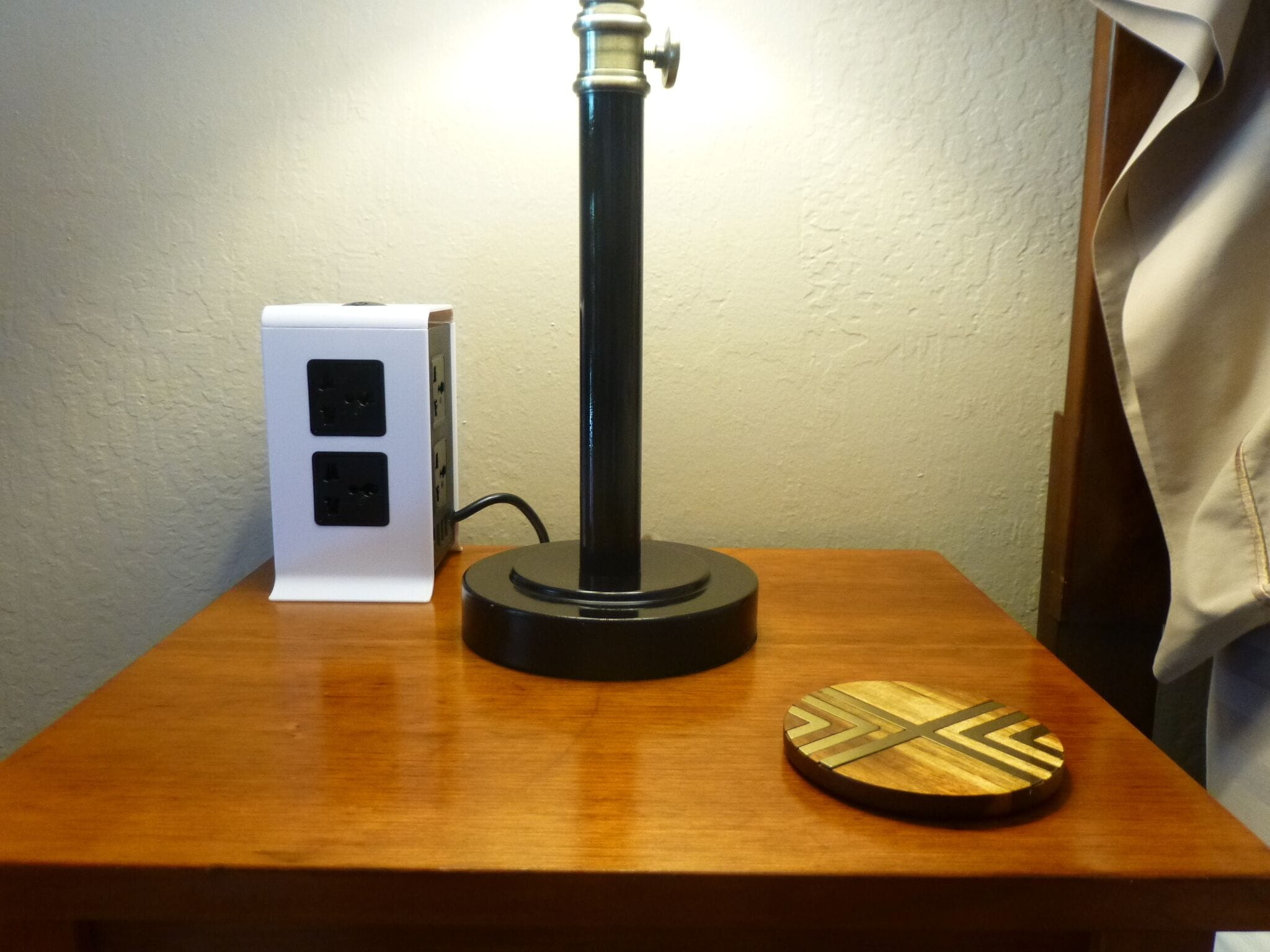 A wooden table with a black lamp, a white electrical box, and a wooden coaster.