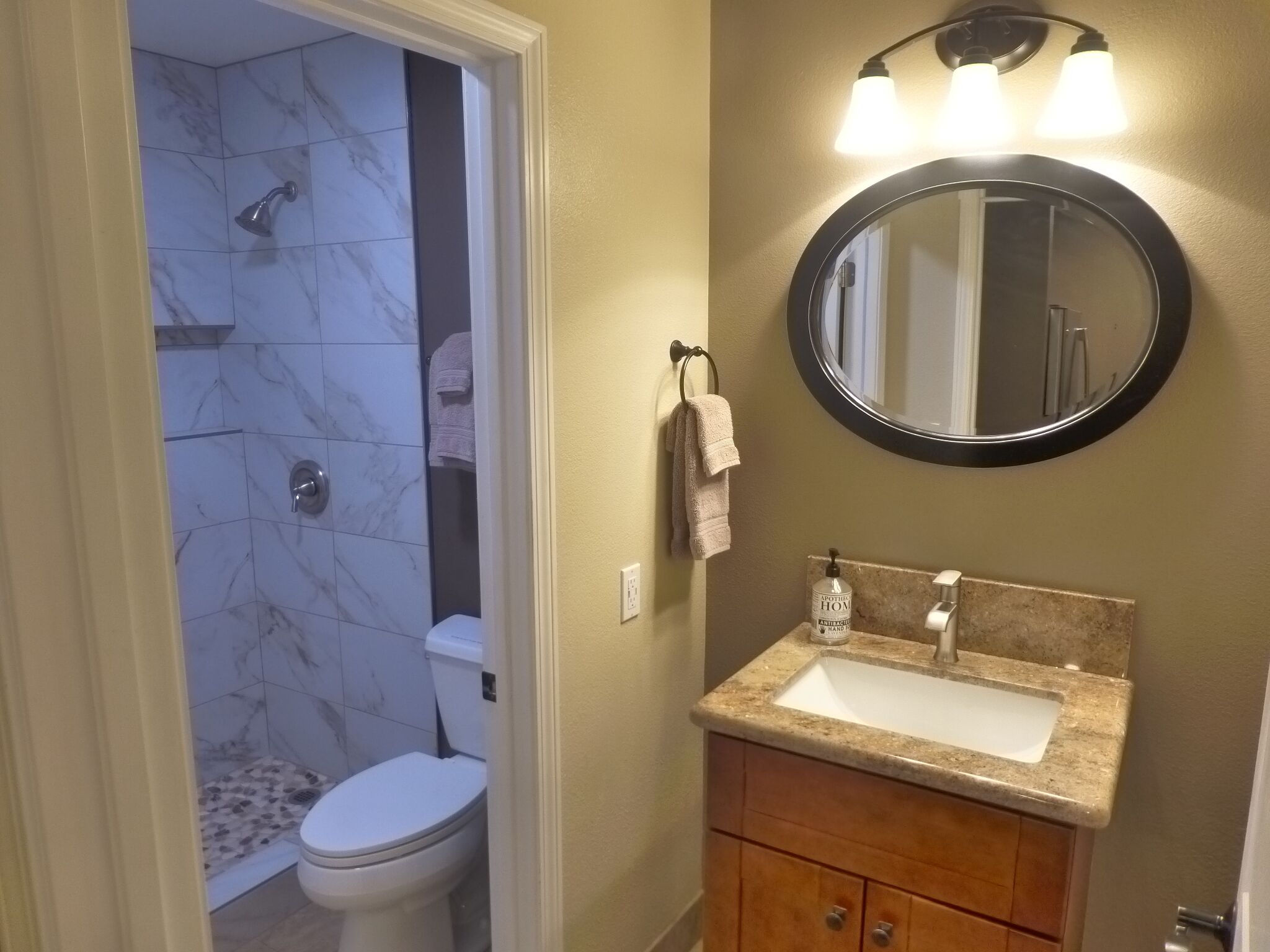 Une salle de bain avec une douche en marbre, des toilettes, un lavabo avec un miroir et une serviette accrochée au mur.