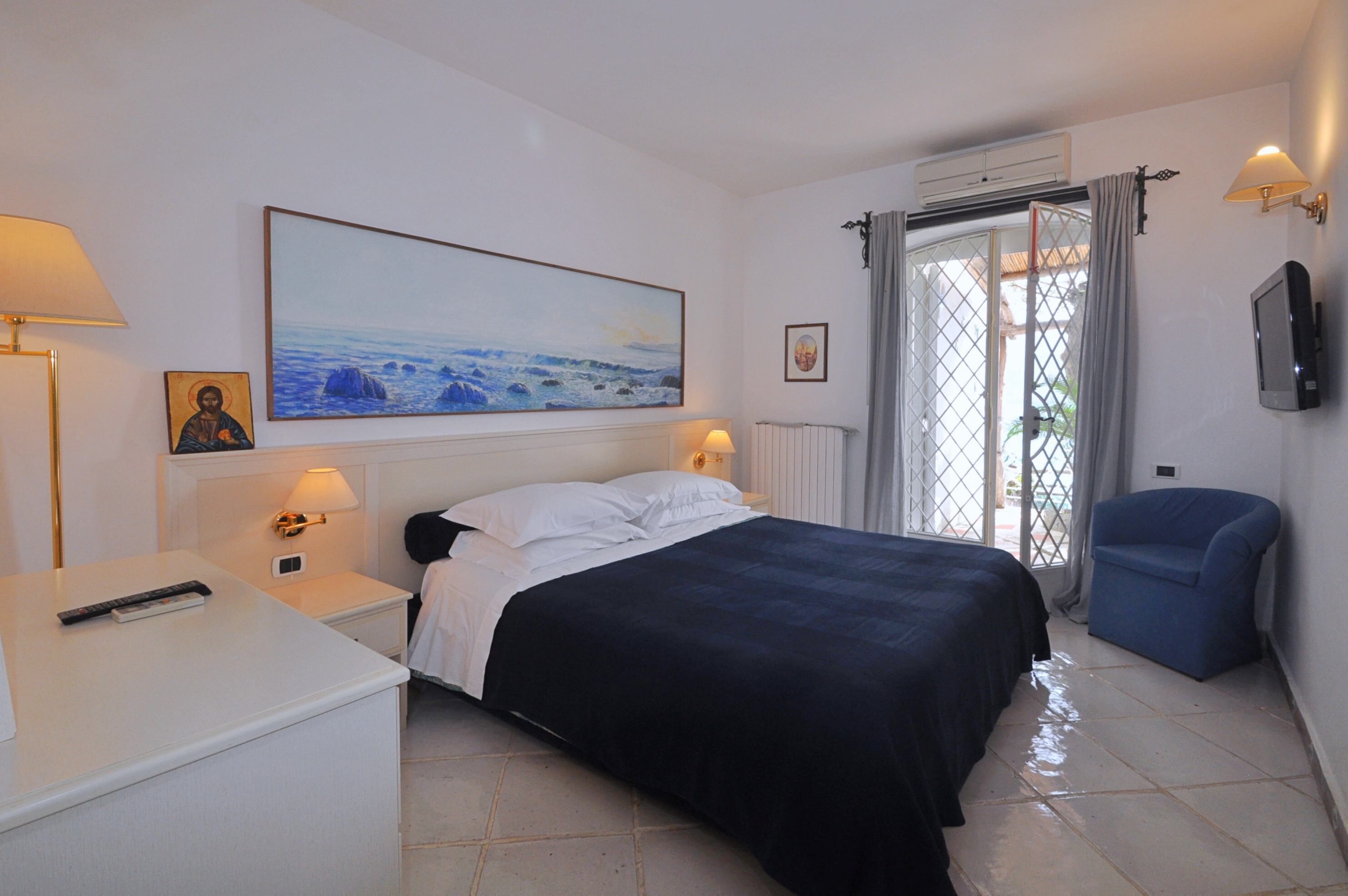 A bedroom with a bed, bedside tables, a desk, a chair, a TV, and a large painting on the wall.