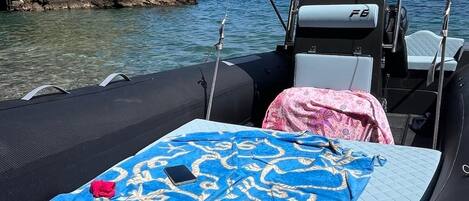 Ein Boot mit überdachtem Sitzbereich, einem kleinen Tisch mit blau gemustertem Tischtuch und einer felsigen Küstenlinie im Hintergrund.