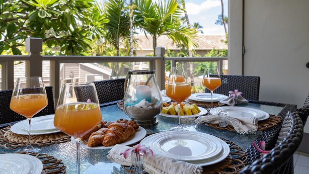 A table set for breakfast with croissants, fruit, and drinks, overlooking a tropical garden. - Hula On In to Beach House Chic Style, Click the Video tour below! (Wailea)
