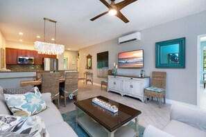 A modern living room with a dining area, a kitchen with stainless steel appliances, and a ceiling fan.