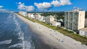 A coastal hotel with a beach view, multiple buildings, and a clear sky.