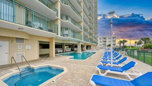 A hotel with multiple swimming pools, outdoor lounge chairs, and a multi-story building with balconies.