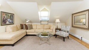 A living room with a sectional sofa, a glass coffee table, a patterned armchair, and a large mirror on the wall. - Desireable Coggeshall Ave - 2-Bdrm Units - 3rd  Floor, sleeps 4 (Newport)