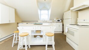 A kitchen with white cabinets, a central island with stools, a microwave, a refrigerator, and an oven. - Desireable Coggeshall Ave - 2-Bdrm Units - 3rd  Floor, sleeps 4 (Newport)
