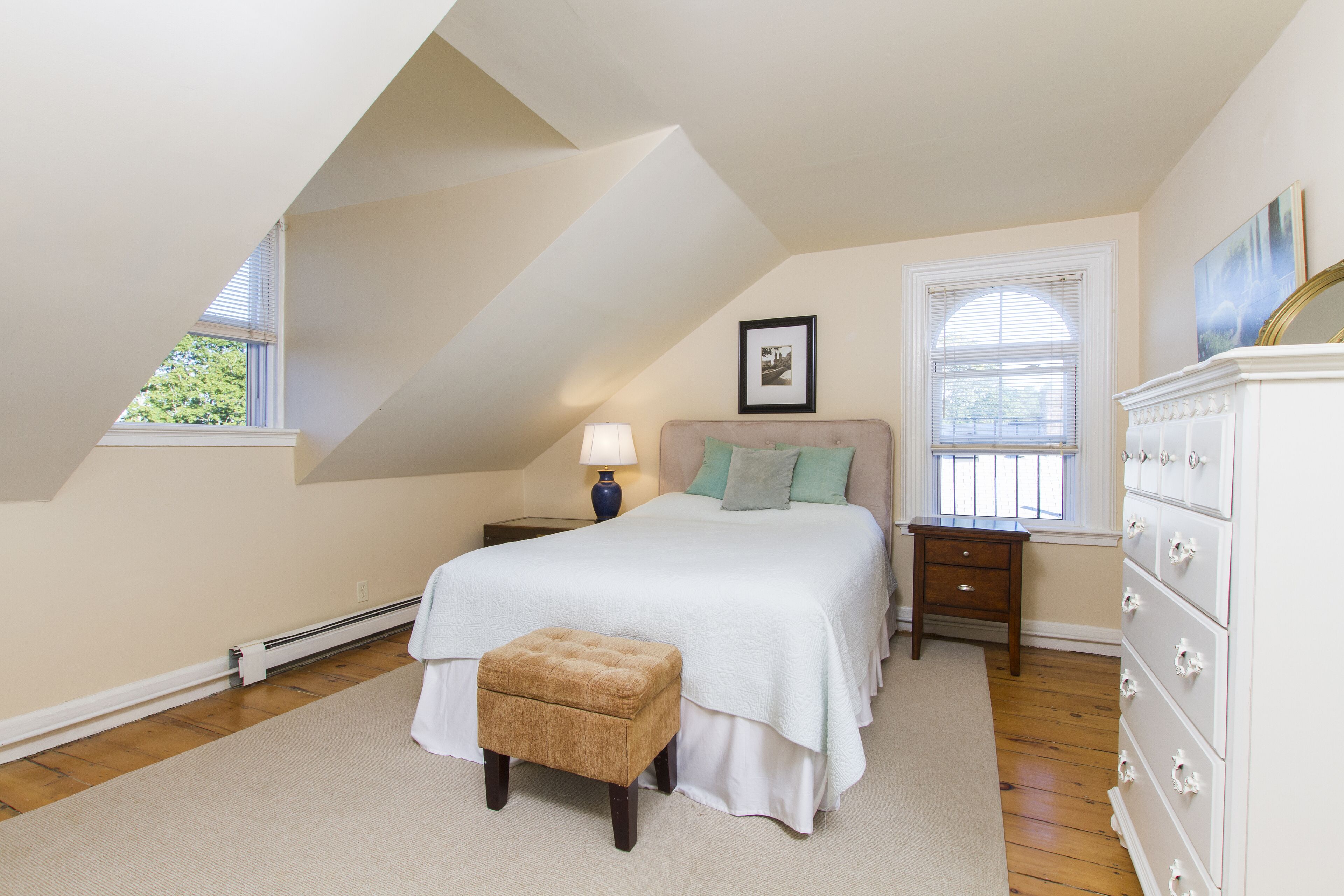 A bedroom with a large bed, a nightstand, a dresser, and a window with blinds.