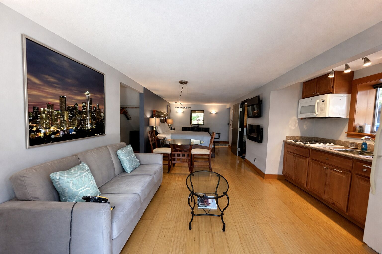 A modern hotel room with a living area, kitchenette, and a cityscape view.