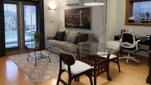Uma sala de estar moderna com uma mesa de jantar de vidro, um sofá, uma poltrona e uma escrivaninha com cadeira.