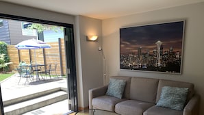 Uma sala de estar com sofá, uma mesa de centro de vidro e uma pintura com vista para a cidade.