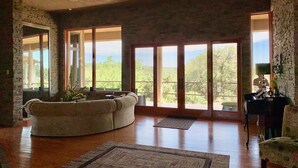 Un salón espacioso con un amplio sofá modular, un piano y vistas a un paisaje exuberante a través de grandes puertas corredizas de vidrio.