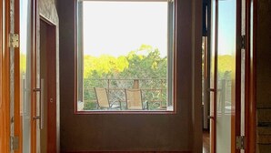 Un pasillo con suelo de madera, un ventanal con vistas a árboles y una puerta a la derecha.