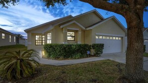 A residential house with a garage, a well-maintained lawn, and a large tree. - The World Villa , South-Facing Pool & Spa , Free Wi-Fi , 3 Miles to Disney (KISSIMMEE)