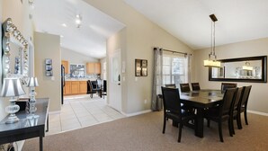 A spacious dining area with a large table and chairs, a kitchen in the background, and a hallway leading to another room. - The World Villa , South-Facing Pool & Spa , Free Wi-Fi , 3 Miles to Disney (KISSIMMEE)