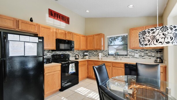 A modern kitchen with wooden cabinets, a black refrigerator, a microwave, and a glass dining table. - The World Villa , South-Facing Pool & Spa , Free Wi-Fi , 3 Miles to Disney (KISSIMMEE)