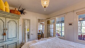 A bedroom with a large bed, a dresser, a chandelier, and a view through a window.