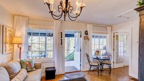 A cozy living room with a sofa, a dining table with chairs, a chandelier, and large windows.