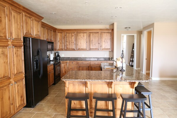A kitchen with wooden cabinets, a black refrigerator, granite countertops, and a central island with bar stools.