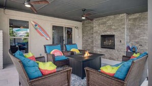 An outdoor patio with wicker furniture, a fire pit, ceiling fans, and a stone wall.