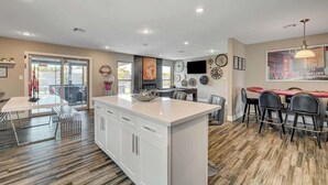 A modern kitchen with white cabinets, a central island, and a dining area with a red table and black chairs.