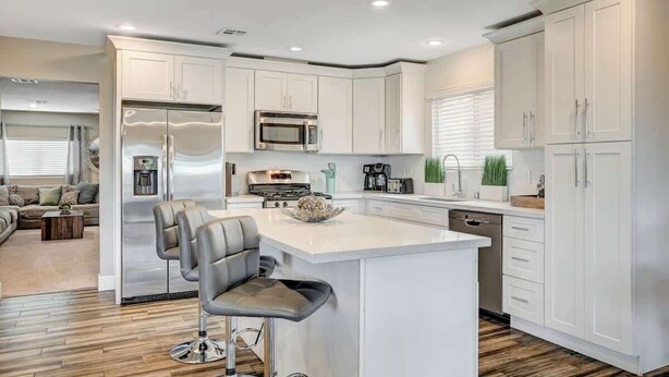 A modern kitchen with white cabinetry, stainless steel appliances, and a central island with bar stools.
