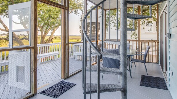 Un espacio exterior techado con una escalera en espiral, ventanas amplias y mobiliario para disfrutar del aire libre.