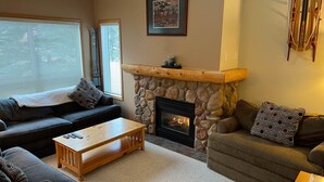A living room with a stone fireplace, a black sofa, a wooden coffee table, and a patterned throw pillow. - Private Hot Tub. Ski In & 15 Minute Walk to the Elk Chair (Fernie)
