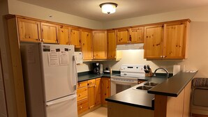 A compact kitchen with wooden cabinets, a white refrigerator, a stove, and a sink. - Private Hot Tub. Ski In & 15 Minute Walk to the Elk Chair (Fernie)