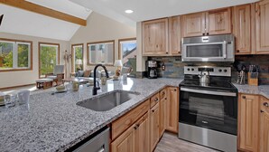 A modern kitchen with granite countertops, stainless steel appliances, wooden cabinets, and a large window offering a view of trees. - Bright, spacious, & extra clean condo in heart of a perfect CO setting! (Keystone)