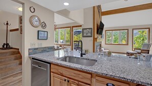 A kitchen with granite countertops, wooden cabinets, and a built-in dishwasher. There are framed pictures on the wall, a clock, and a window with a view of trees. - Bright, spacious, & extra clean condo in heart of a perfect CO setting! (Keystone)
