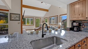 A kitchen with granite countertops, a stainless steel sink, wooden cabinets, and a dining area with a view of trees. - Bright, spacious, & extra clean condo in heart of a perfect CO setting! (Keystone)