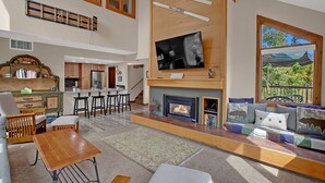 A spacious living area with a fireplace, a television mounted on the wall, and a view of the outdoors through a window. - Bright, spacious, & extra clean condo in heart of a perfect CO setting! (Keystone)